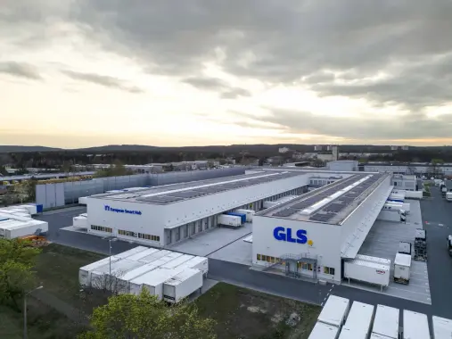 GLS-paketteja ja GLS-työntekijä on iloisena taustalla.