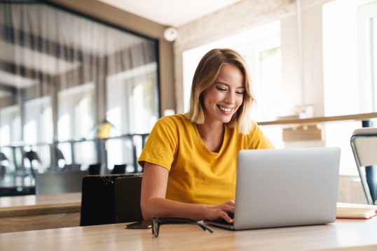 Femme souriante travaillant sur son ordinateur portable, gérant son compte YourGLS depuis son bureau