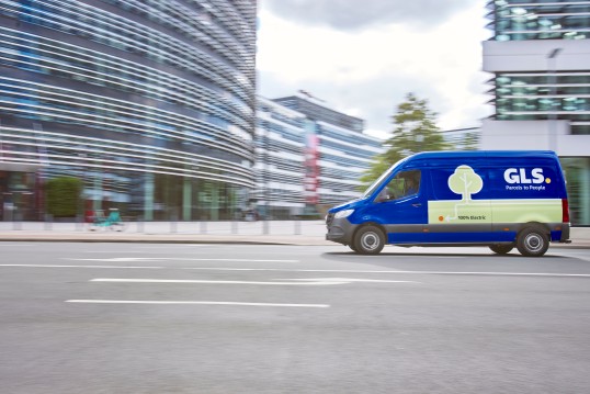 GLS driver smiling while holding a parcel in front of an open delivery van