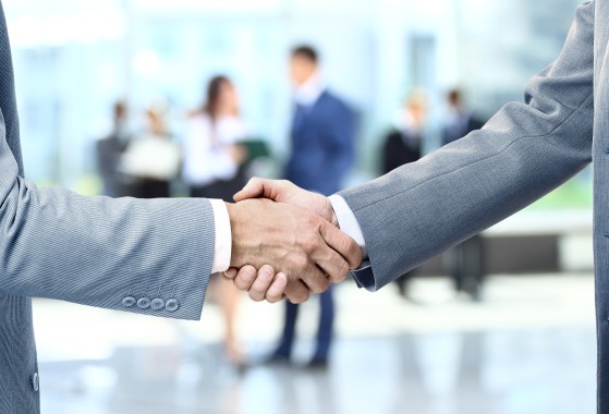Hands reaching out for a business handshake in front of a professional setting.